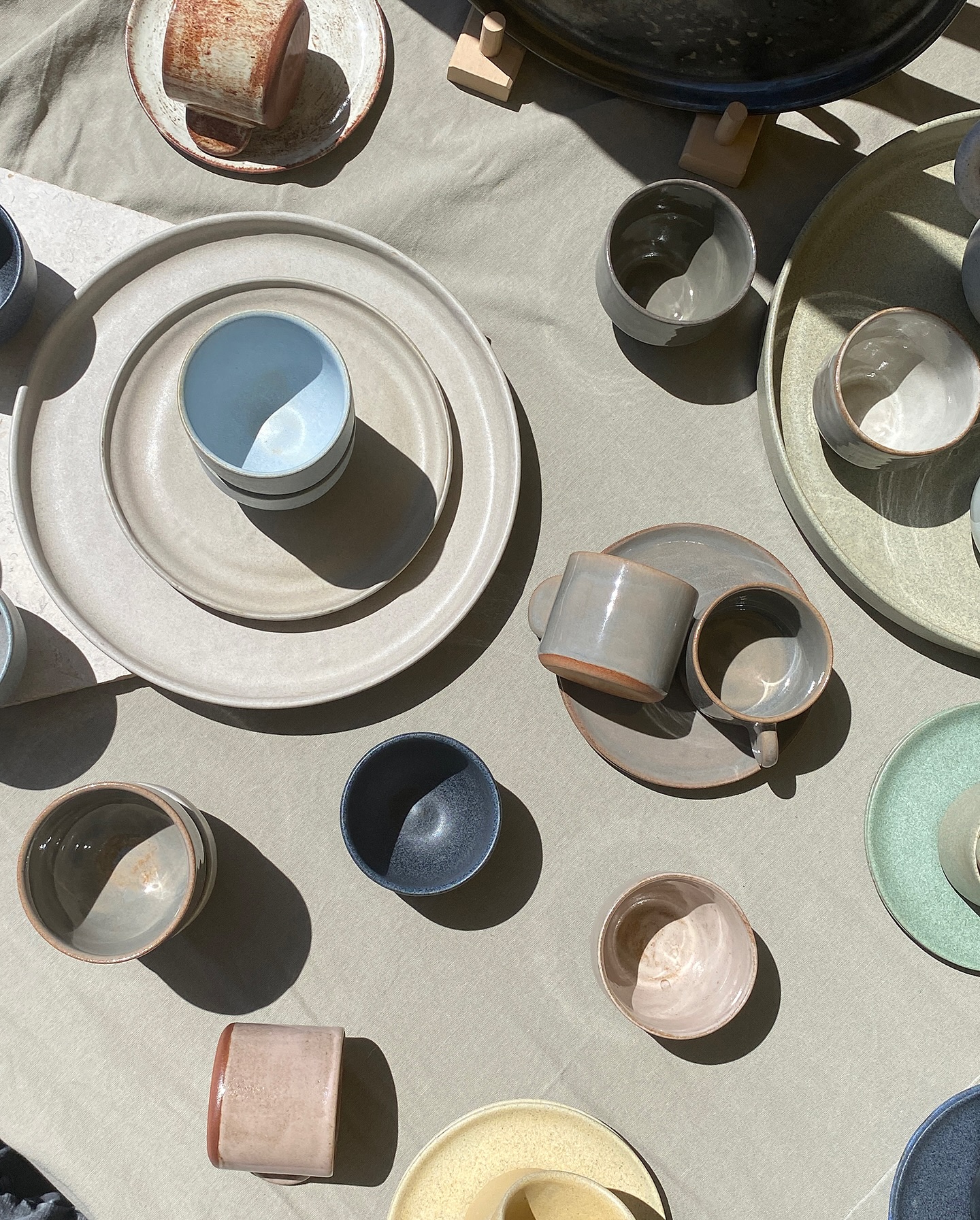 A table laid with stoneware cups, plates and bowls in soft daylight